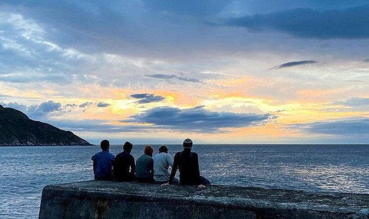 Fem personer sitter med ryggen til og stirrer ut på en solnedgang over havet.